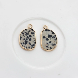 Close-up of natural Dalmatian Jasper pendants with gold plated edges on white ceramic