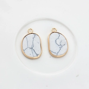 Detail of two irregular white turquoise pendants with gold plated frames on white ceramic