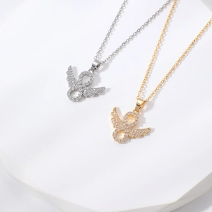 Infinity wing pendant necklace with pavé stones in gold and silver finishes on stone pedestal
