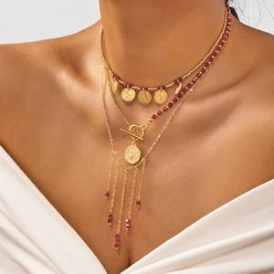 Détail d'un collier bohème multicouche avec cristaux rouges, pièces et pompons