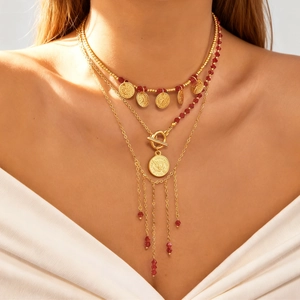 Détail du collier multicouche en or avec perles rouges et pendentif à pampilles