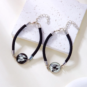 Close-up of woven couple bracelets with butterfly glass pendants on a textured stone
