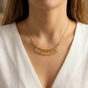 Détail d'un collier doré multicouche avec pampilles de pièces et texture en relief