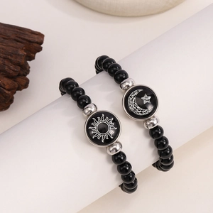 Detail of sun and moon charm beaded bracelets on a white pedestal for couples