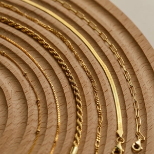 Detail of diverse gold-plated chain styles on a wooden display tray for jewelry collection