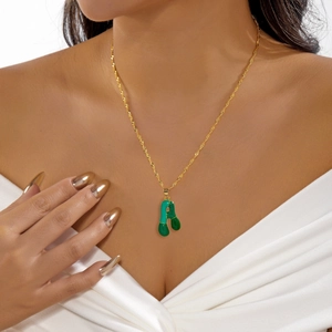 Dettaglio di una catena a corda dorata con pendente a lettera A in smalto verde su modella