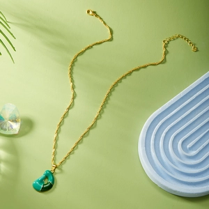 Dettaglio della collana dorata con ciondolo a cuore in smalto verde e chiusura a moschettone