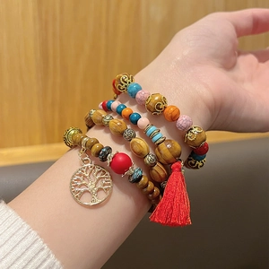 Détail du bracelet bohème multicouche en perles de bois avec pendentif arbre et pompon rouge