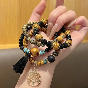 Détail de bracelet multicouche bohème avec perles en bois, arbre de vie et pompon noir