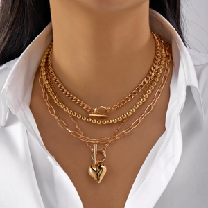 Detail of layered gold OT buckle necklace with heart pendant on a model wearing white shirt