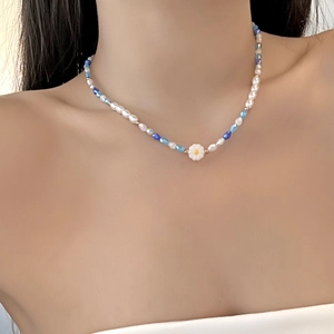 Close-up of beaded necklace with blue faceted gems, white pearls and a daisy pendant