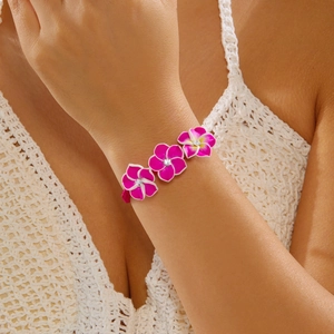 Detail eines handgewebten Armbands mit rosa Frangipani-Blüten und funkelnden Strasssteinen