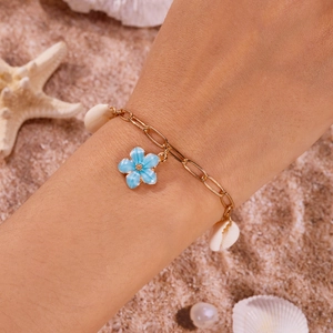 Bohemian gold ankle bracelet with blue flower pendant and white shells on beach