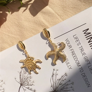 Detalle de pendientes dorados de estrella de mar y tortuga sobre playa de arena