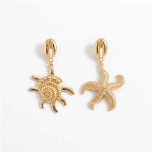 Detalle de pendientes dorados de concha y estrella de mar con dijes asimétricos