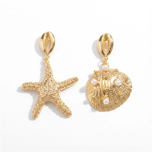 Detalle de pendientes asimétricos dorados con estrella de mar, concha y perlas