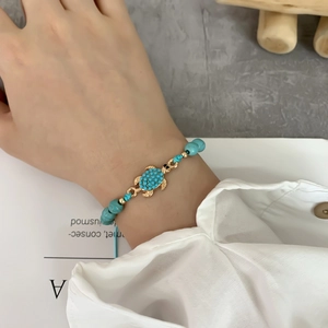 Dettaglio del bracciale con tartaruga dorata e perline blu indossato sul polso
