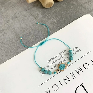 Dettaglio del bracciale intrecciato turchese regolabile con ciondolo a tartaruga dorata