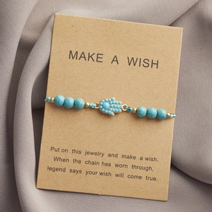Dettaglio della mano di Fatima e perline blu su carta Make A Wish su tessuto grigio