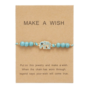 Dettaglio del bracciale blu intrecciato con ciondolo a elefante dorato su cartoncino regalo