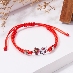 Dettaglio del bracciale rosso intrecciato con ciondolo a farfalla e perline d'argento