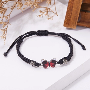 Dettaglio del bracciale in corda nera intrecciata con ciondolo a farfalla rossa e nodo