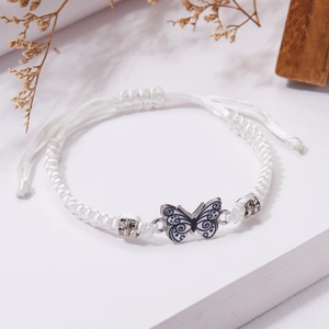 Dettaglio del bracciale intrecciato bianco con ciondolo a farfalla e perline con diamanti