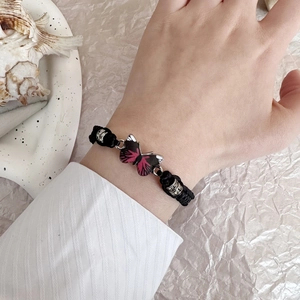 Dettaglio del bracciale in corda nera intrecciata a mano con farfalla rosa e perline
