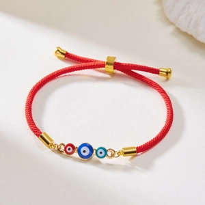 Detail eines roten geflochtenen Evil Eye Armbands mit drei Anhängern und Schiebeverschluss