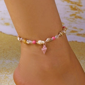 Detail of seashell anklet with pink beads and conch pendant on a sandy beach