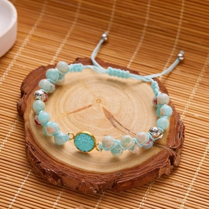 Detalle de pulsera tejida a mano con piedras azul claro y dije con borde dorado