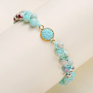 Primer plano de pulsera tejida a mano con piedras naturales azul claro y dije de cristal