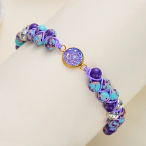 Detalle de pulsera tejida a mano con piedra druzy púrpura y cuentas metálicas florales