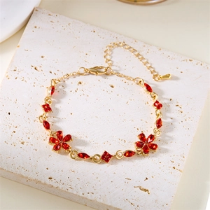 Details eines goldenen Blumenarmbands mit roten Kristallen auf weißem Stein