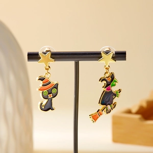 Macro detail of asymmetric Halloween earrings featuring a black cat and flying witch charms