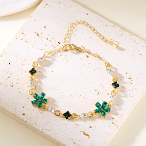 Goldenes Blumenarmband mit Smaragd und Kristallsteinen auf strukturierter Steinplatte