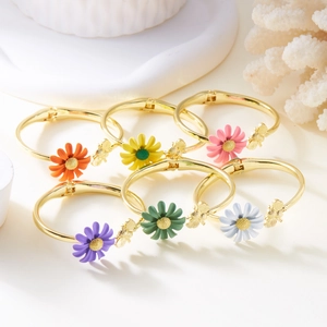 Detail van kleurrijke emaille madeliefjes en vlinderhanger op gouden armbanden met veer