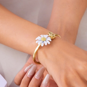 Detail van een gouden open armband met wit madeliefje en kleine bij op de pols