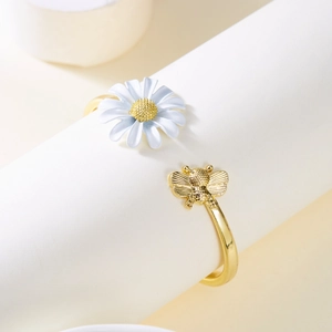 Detail van een gouden open armband met witte madeliefje en gouden bij elementen