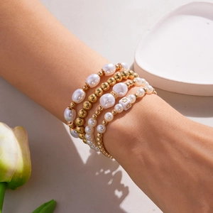 Detail van vierdelige parel- en gouden kralenarmbandset met bloemenbedels om de pols