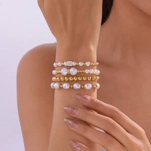 Detailweergave van een vierdelige armbandset met witte parels en gouden metalen kralen