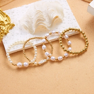 Detailopname van een vierdelige armbandset met witte parels en gouden kralen op een schelp