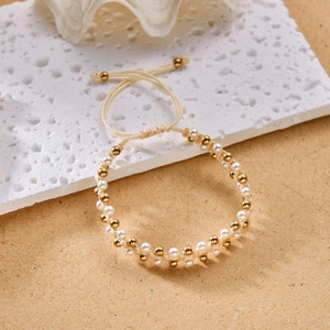 Detail van de handgeweven beige armband met witte parels en gouden kralen