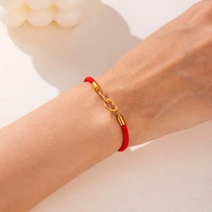 Detail of red braided cord bracelet featuring interlocking golden heart clasps on wrist
