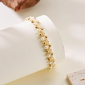 Detail van geweven armband met witte parels en gouden kralen op een witte display
