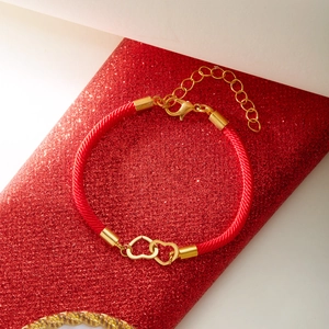 Macro detail of red woven rope bracelet with interlocking gold heart pendants and lobster clasp
