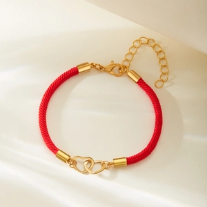Macro shot of red braided rope bracelet with interlocking golden heart charms in sunlight
