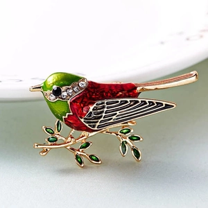 Elegant bird brooch on golden branch with green and red enamel and sparkling crystal accents