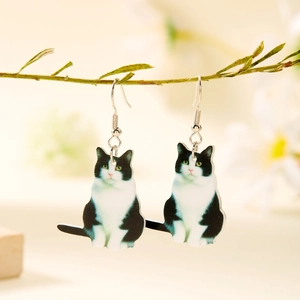 Dettaglio di orecchini pendenti gatto bianco e nero in acrilico appesi al ramo