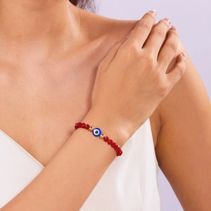 Detail van rode gefacetteerde kristallen armband met blauw boze oog om de pols gedragen